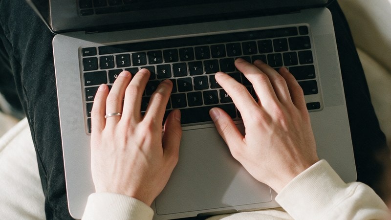 Manos escribiendo en una laptop.